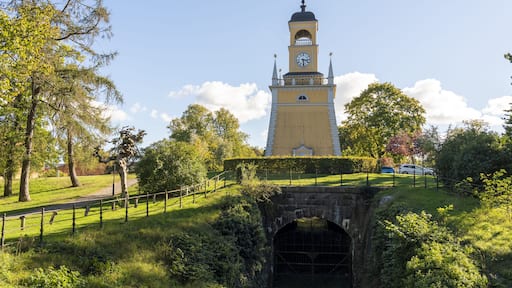 Un clocher abritant une horloge, entouré de verdure et surplombant un pont de pierre.