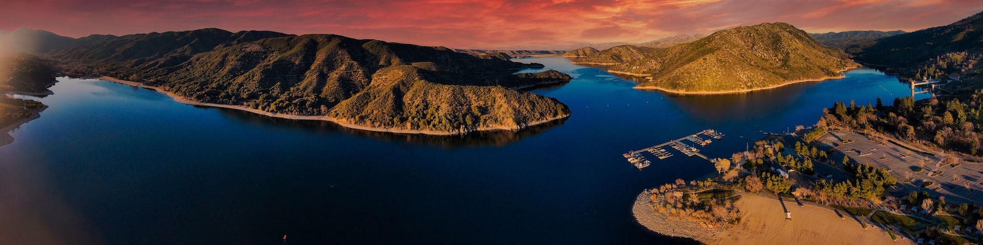 a majestic aerial panoramic shot of the vast blue still lake water with breathtaking mountain ranges reflecting off the lake at sunset at Silverwood Lake in San Bernardino County, California
