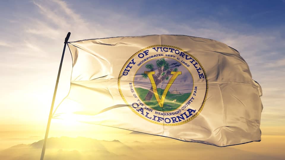 A flag with the emblem of the City of Victorville, California, featuring palm trees and a mountain landscape.