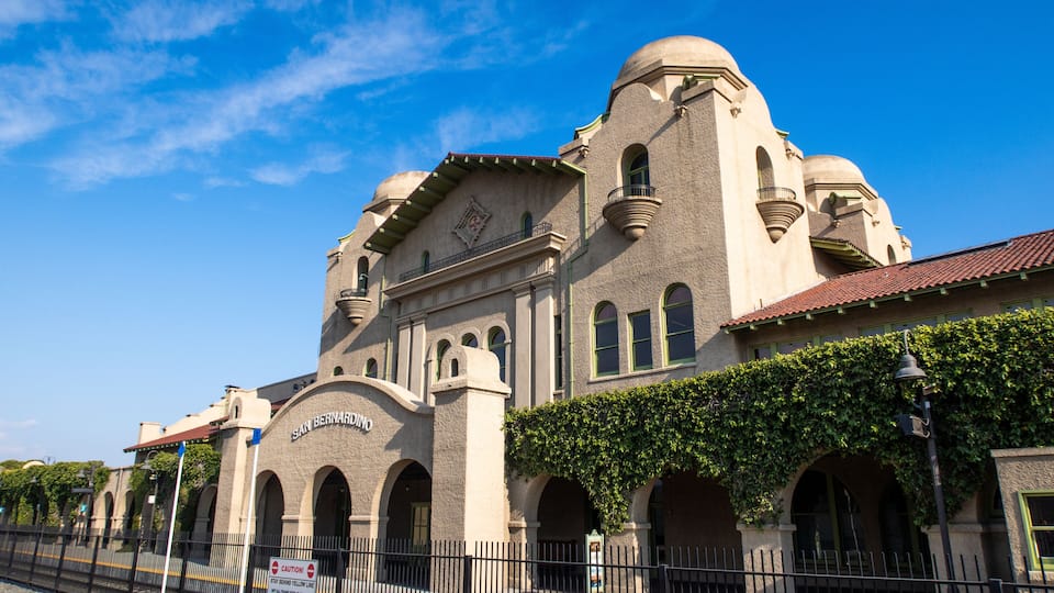 A historic building with arched windows and a dome, surrounded by a fence and greenery.