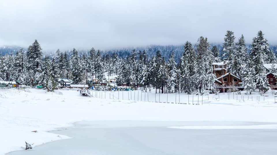 A snowy landscape with a frozen lake, snow-covered trees, and wooden cabins.