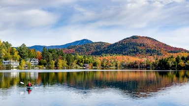 A calm lake with a kayaker, autumn-colored trees, and a mountain in the background.