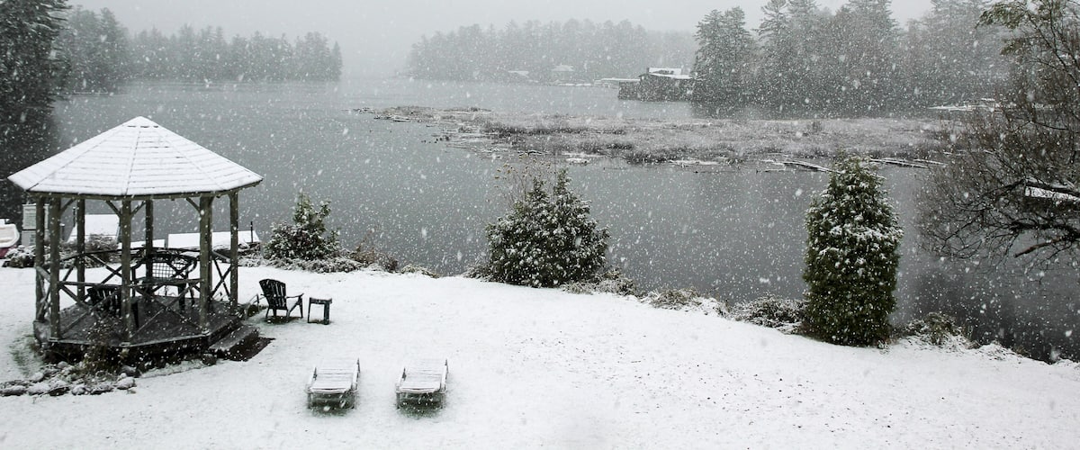 A gazebo, snow-covered chairs, a snow-laden tree, and a lake.