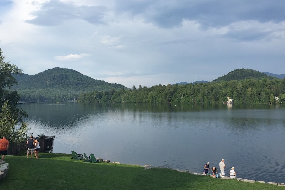 A calm lake surrounded by green hills and a cloudy sky.