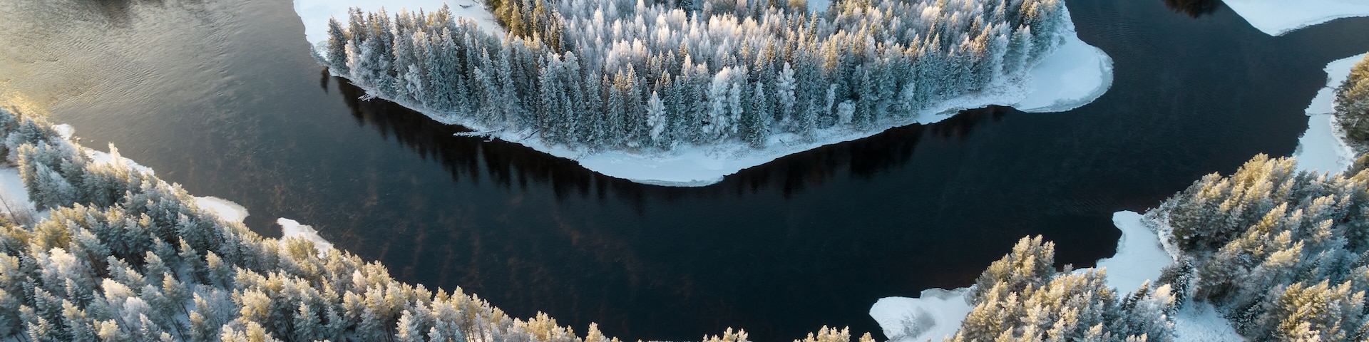 Aerial view of snowy winter forest with black river. Drone photography - panoramic image of beautiful frosty trees and loops of river in Jamtland County, Sweden