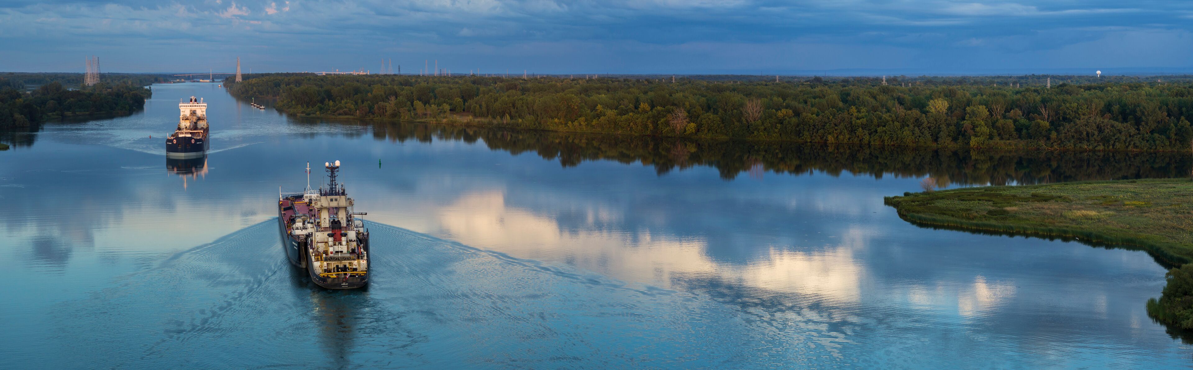 A river with two cargo ships and a bridge in the background.