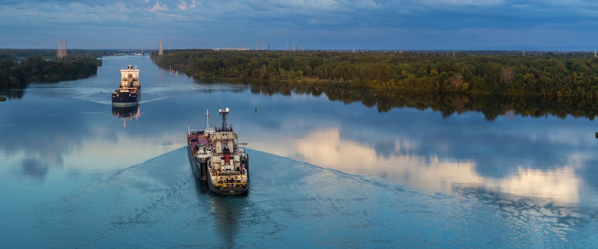 A river with two cargo ships and a bridge in the background.