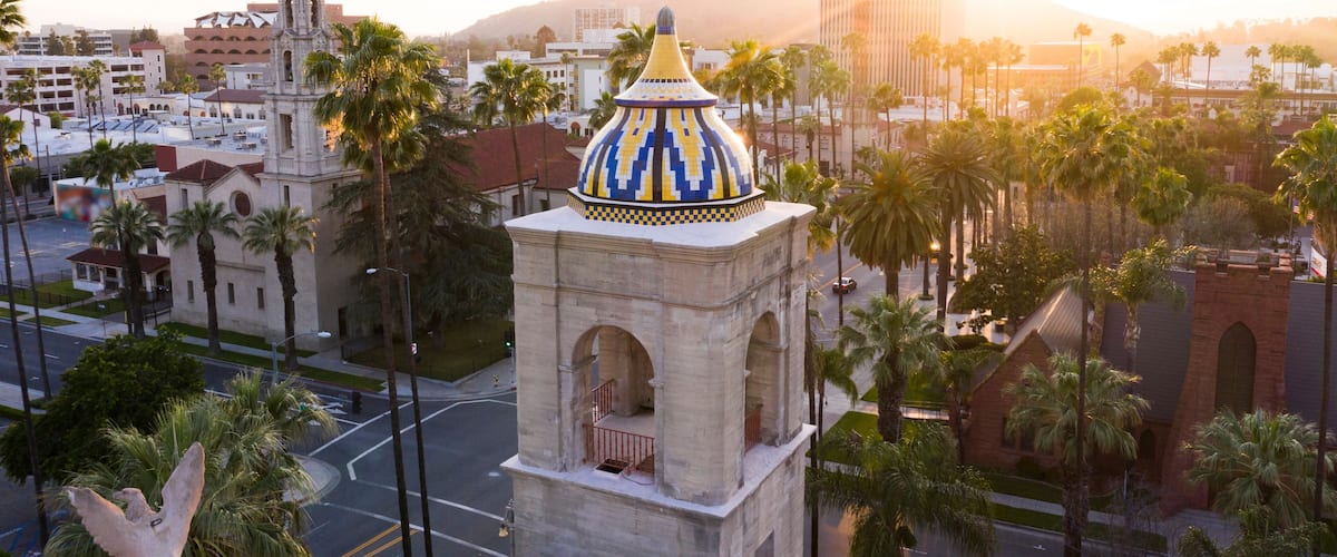 A cityscape with a prominent tower featuring a colorful dome, surrounded by palm trees and urban buildings.
