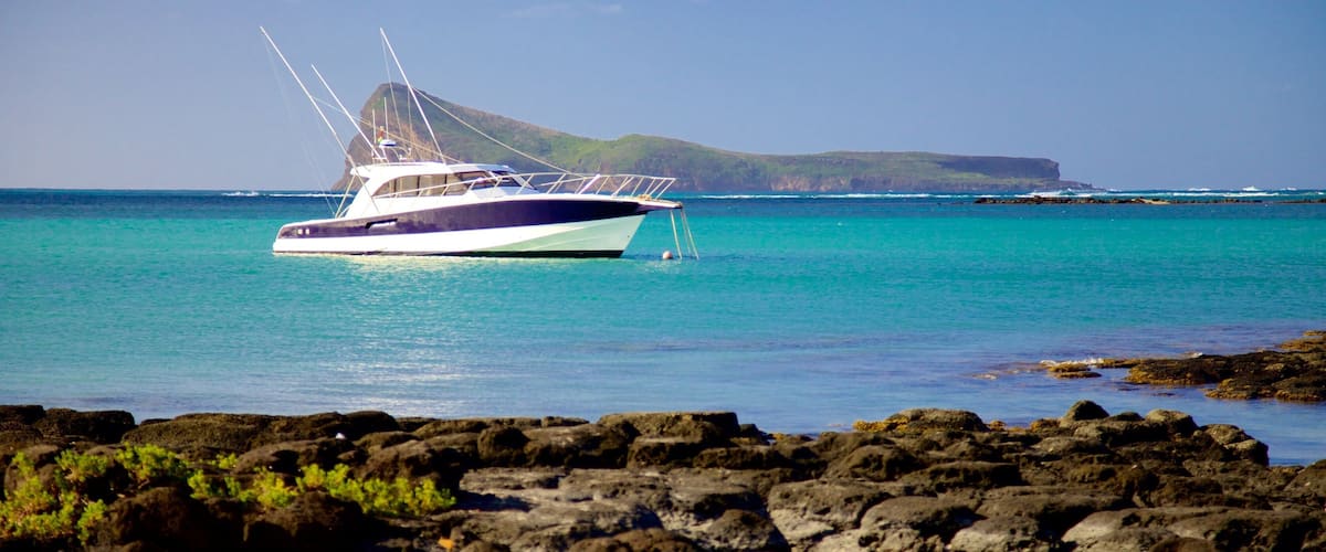 A boat on turquoise water with rocky coastline and a distant island.