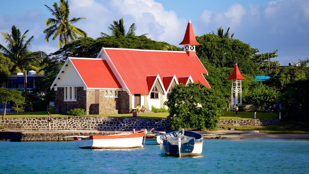 Un bâtiment situé sur la côte, avec un toit rouge, un mur en pierre et des bateaux sur l’eau.