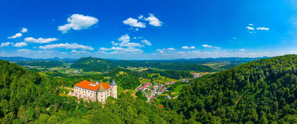 A castle surrounded by lush green forests and rolling hills under a clear blue sky.