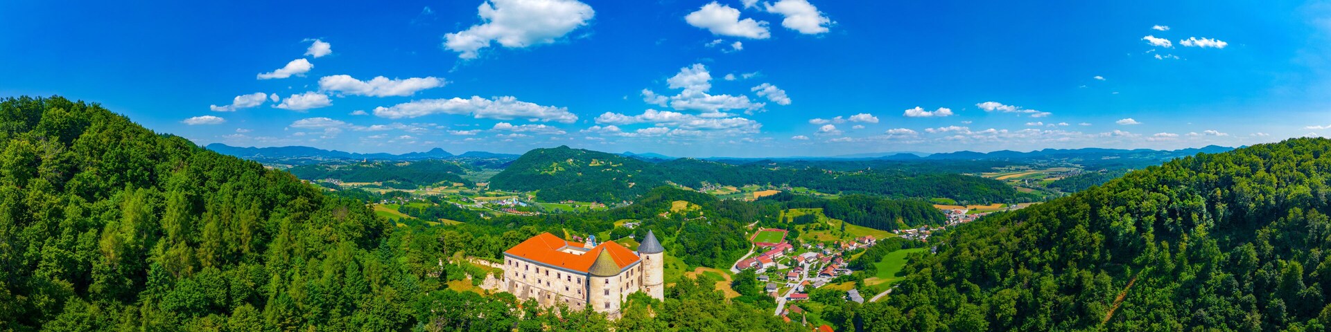 A castle surrounded by lush green forests and rolling hills under a clear blue sky.