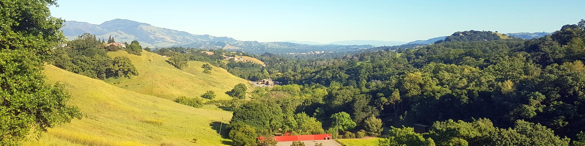 Rolling green hills, a red-roofed building, and a valley with dense forests.
