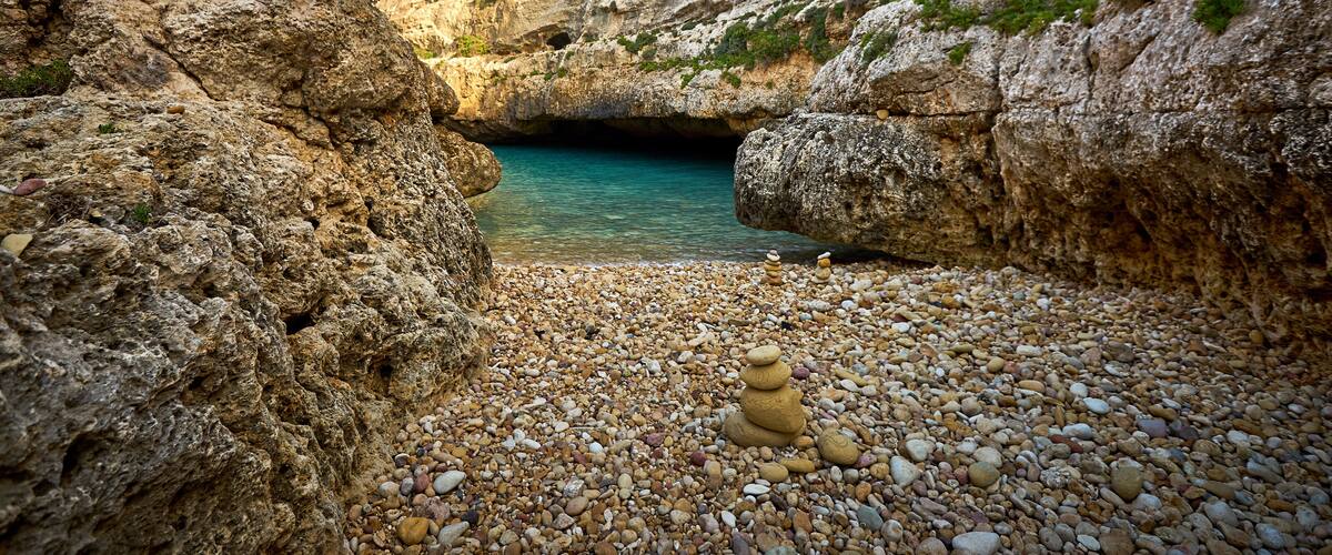 A rocky landscape with a clear blue sky, a turquoise water body, and a stack of stones.