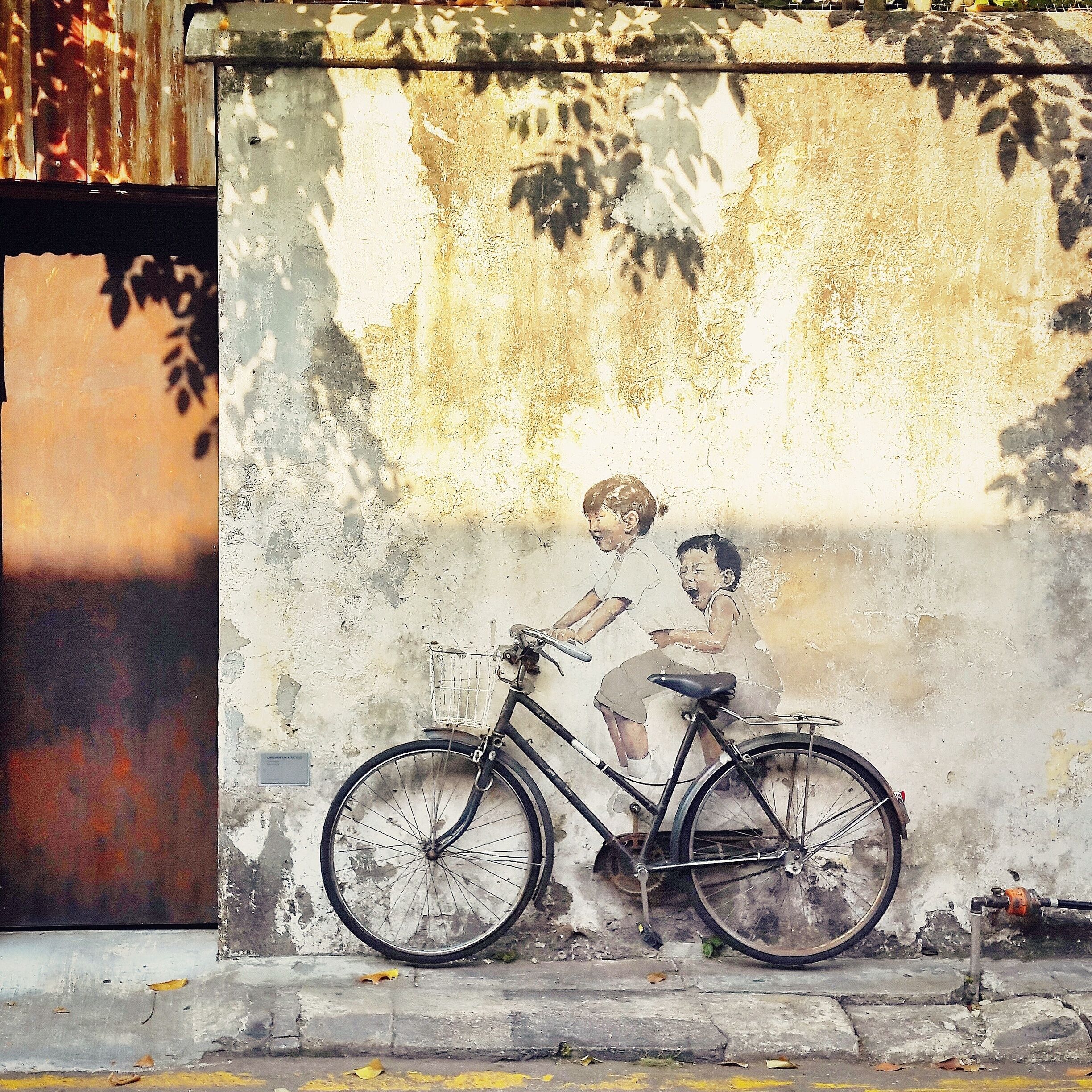 A mural of two children on a bicycle, a worn wall, and a metal structure in the background.