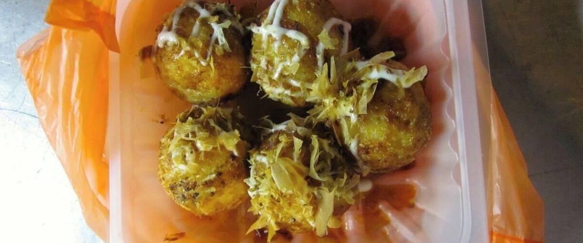 A container with food items, possibly fried balls, garnished with shredded ingredients.