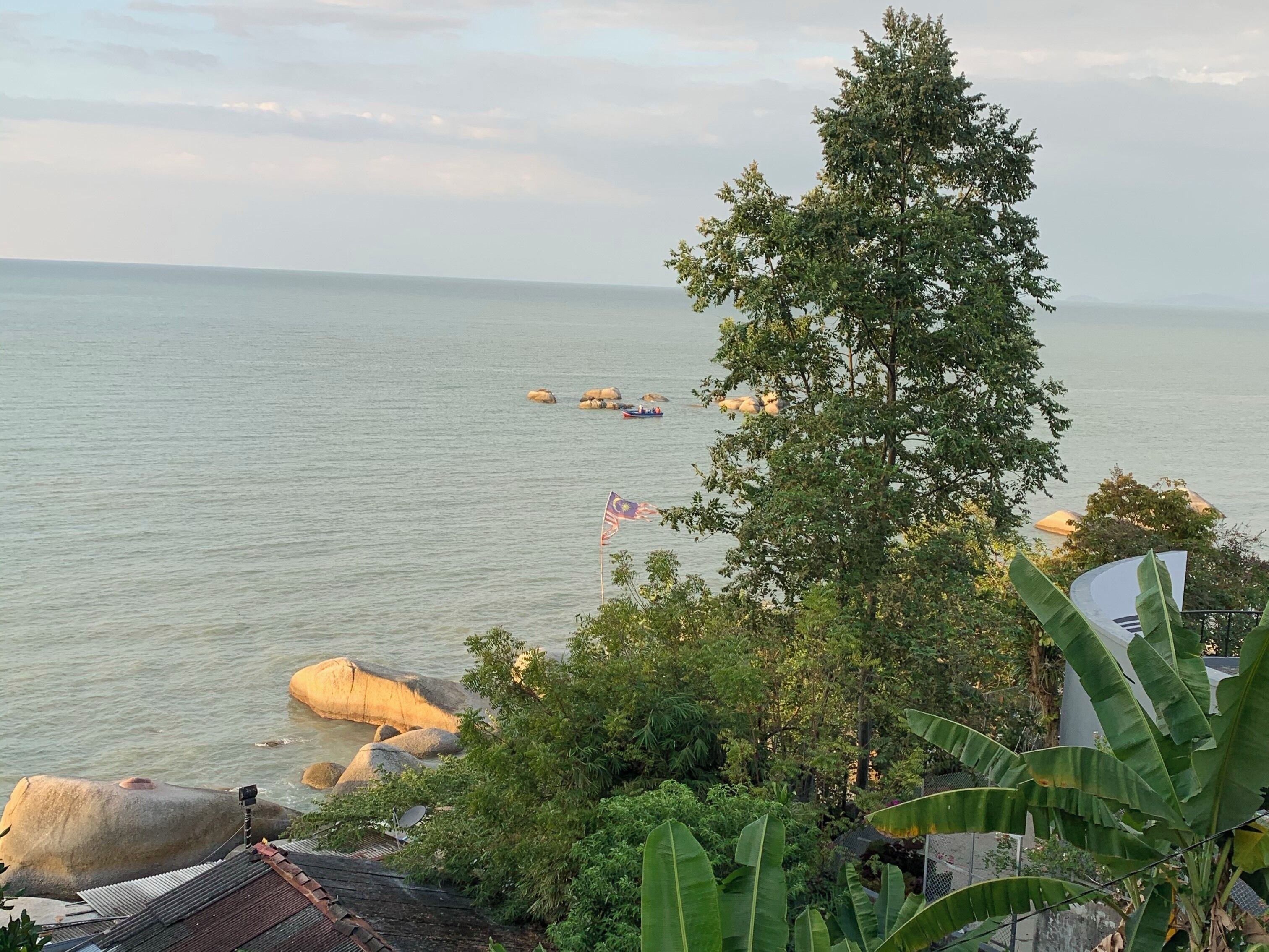 A coastal landscape with a view of the sea, large rocks, and a flag-raising ceremony.