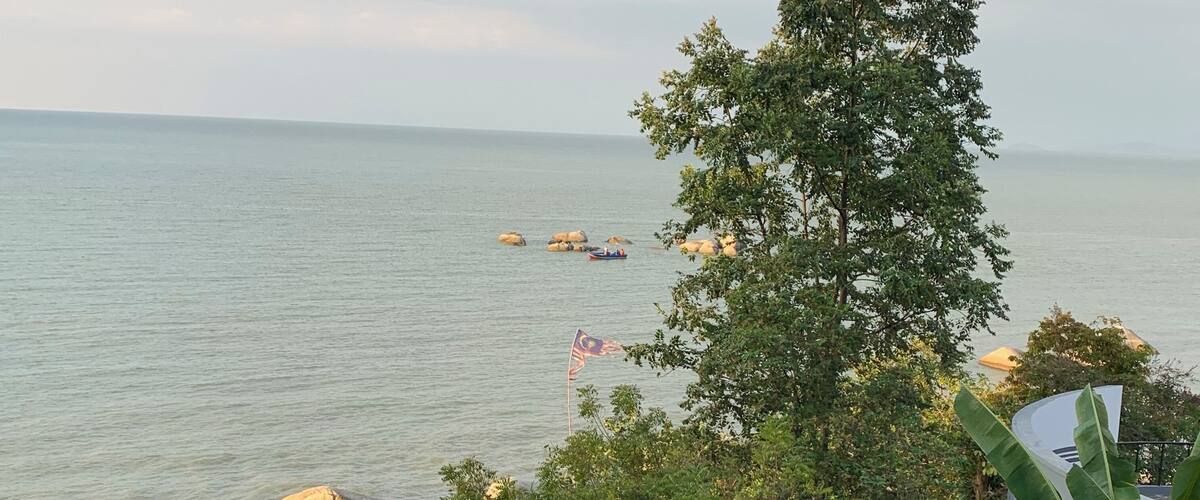 A coastal landscape with a view of the sea, large rocks, and a flag-raising ceremony.