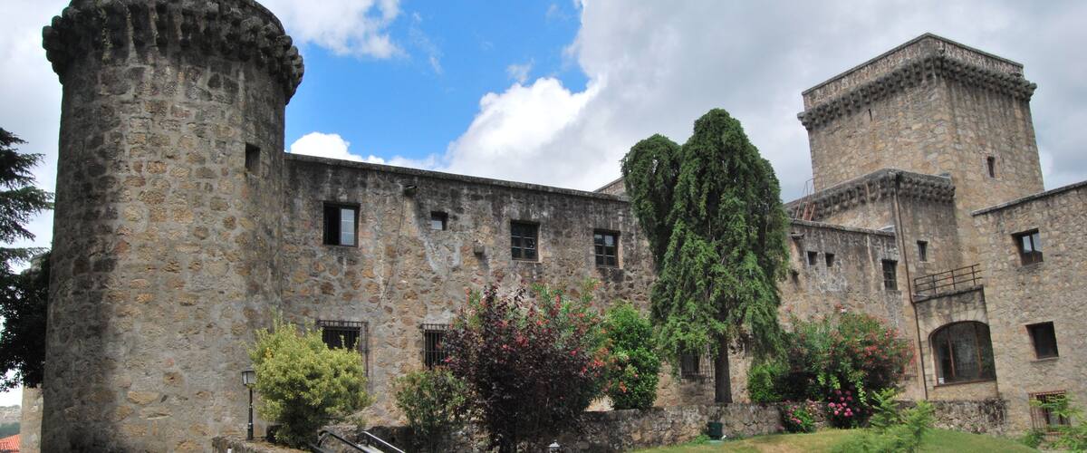 A historic stone building with a round tower and a square tower, surrounded by a well-maintained lawn and trees.