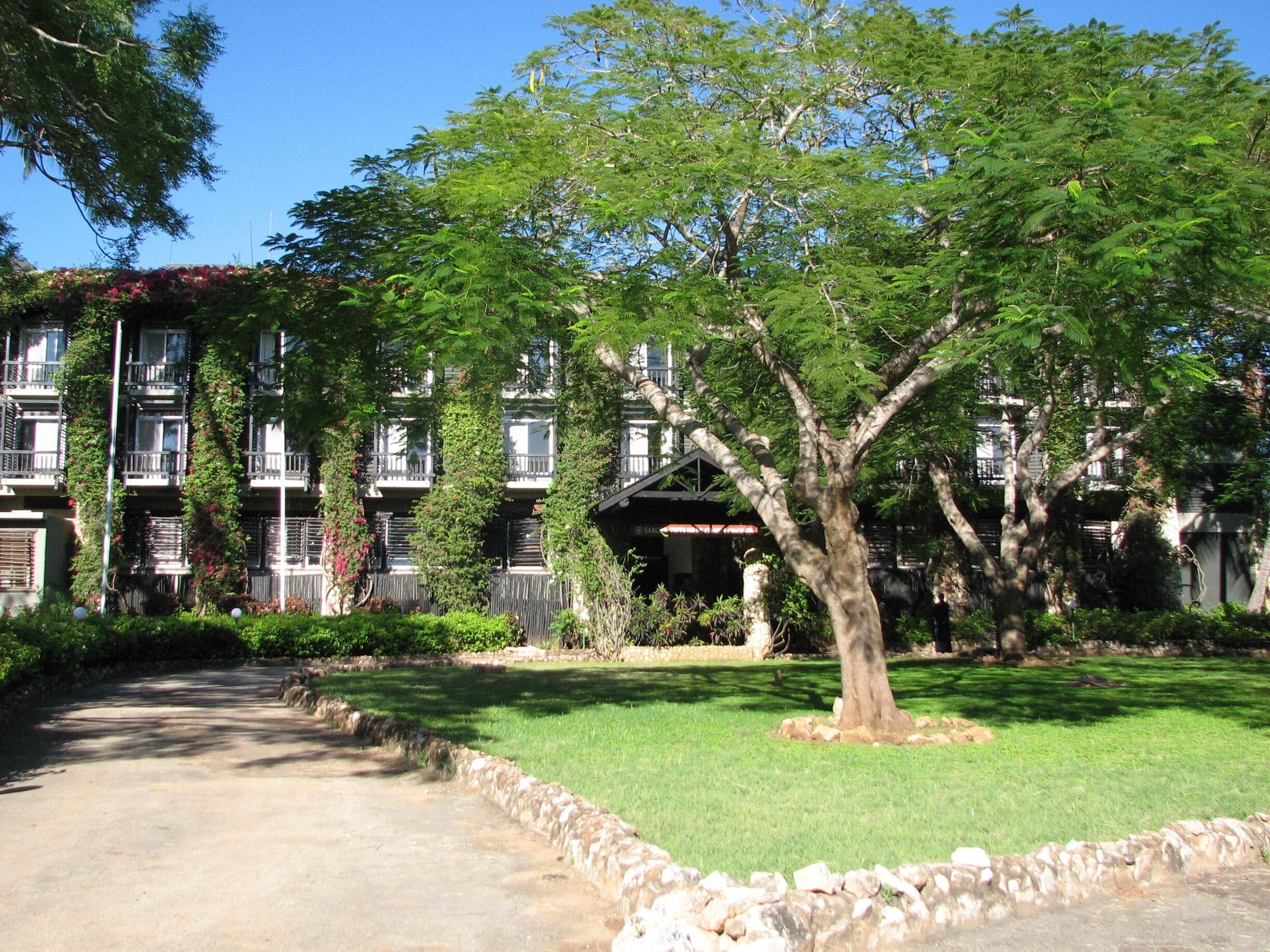 A building with multiple balconies, surrounded by lush greenery and a well-maintained lawn.