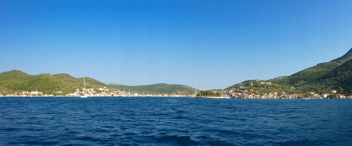 A coastal town with a clear blue sky, surrounded by green hills and a calm sea.
