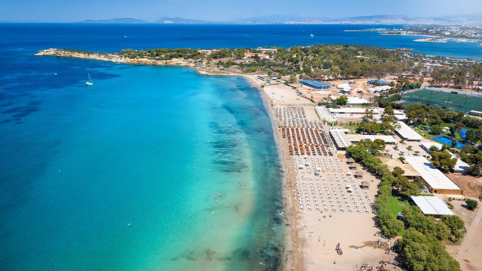 A coastal town with a beach, clear blue waters, and a distant mountain range.