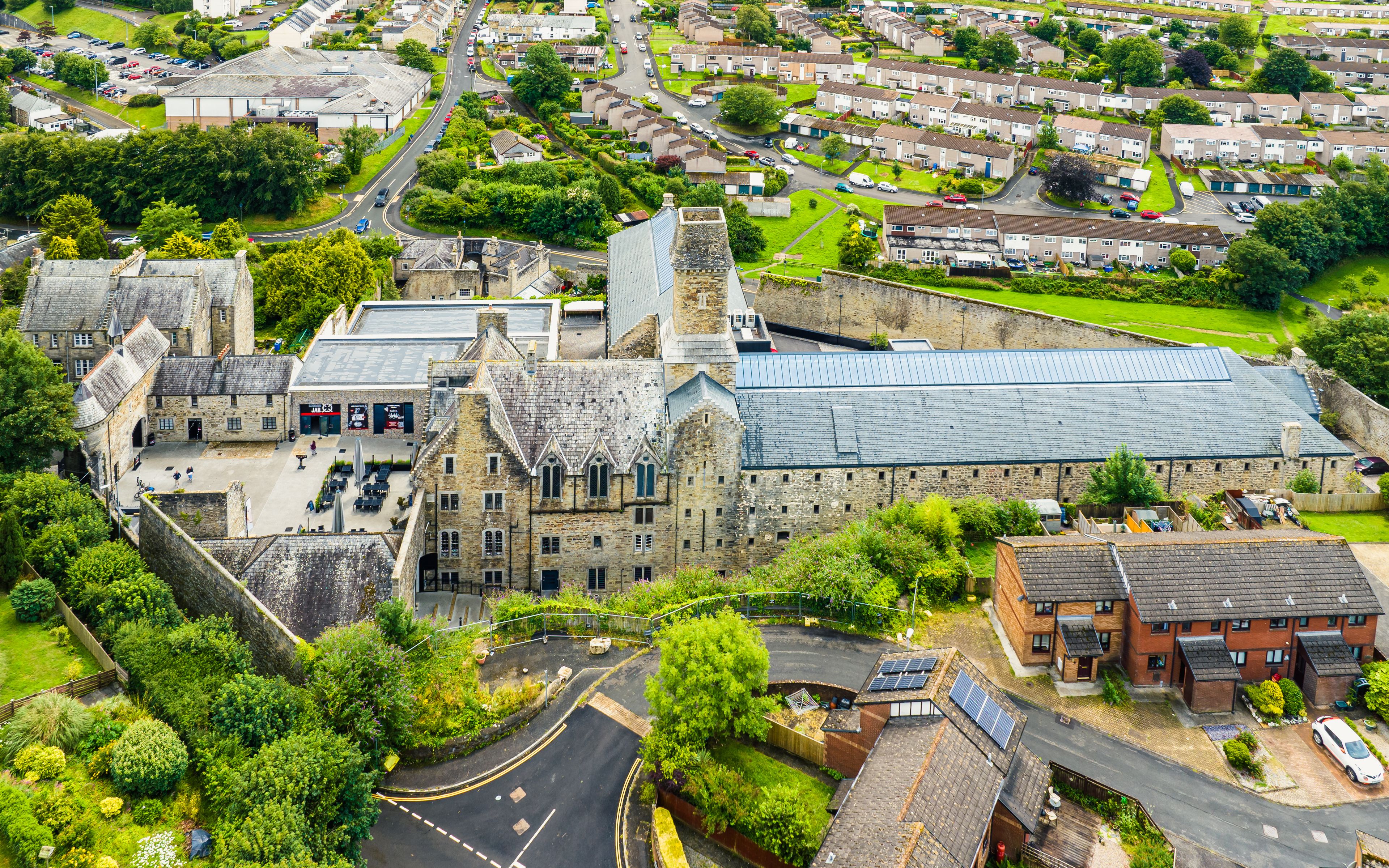 An aerial view of a historic stone building with a large courtyard, surrounded by residential houses and greenery.