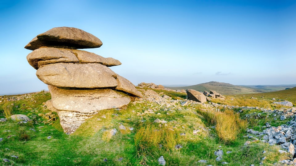 A stack of large boulders in a grassy field with rolling hills in the background.