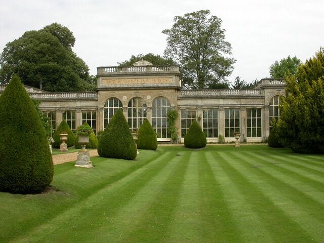 Un jardín formal con setos bien cuidados y un edificio clásico con ventanas arqueadas.