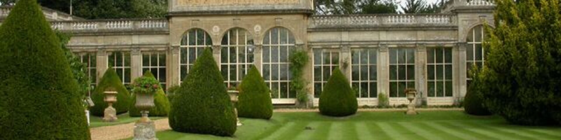 Un jardín formal con setos bien cuidados y un edificio clásico con ventanas arqueadas.