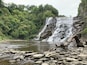 Una cascada de varios niveles rodeada de abundante vegetación y terreno rocoso.