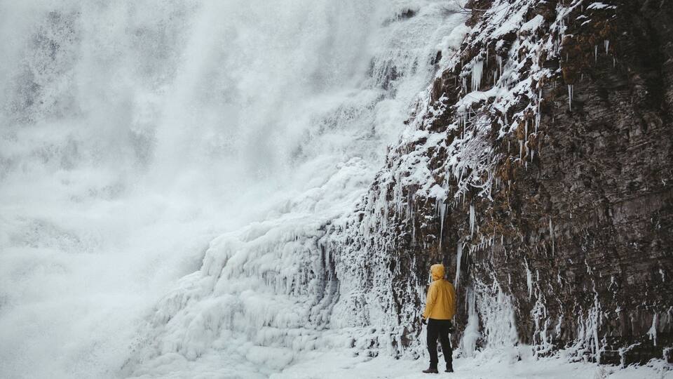 A person in a yellow jacket standing in front of a waterfall with ice formations.