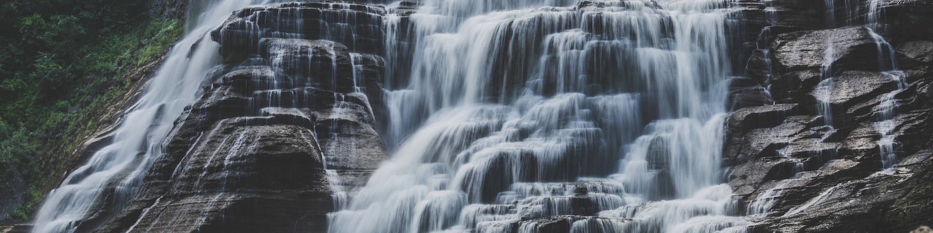 Una cascada escalonada que se precipita sobre formaciones rocosas oscuras, rodeada de exuberante vegetación.
