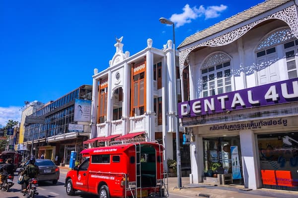 A street with a red three-wheeled vehicle, a building with a dental clinic, and a hotel.