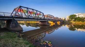 Uma ponte com bandeiras coloridas, um rio calmo e edifícios ao fundo.