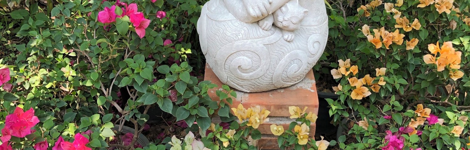 Un jardín con una estatua de Buda de piedra rodeada de flores coloridas y abundante vegetación.