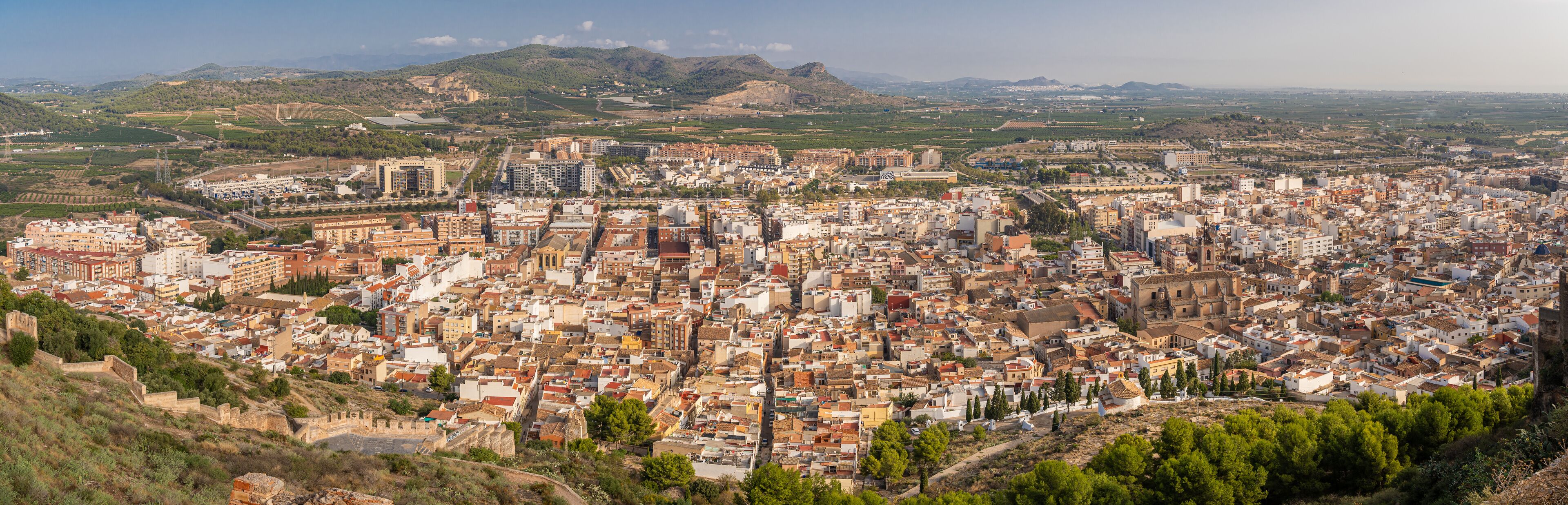 A densely packed cityscape with historical architecture, surrounded by hills and fields.