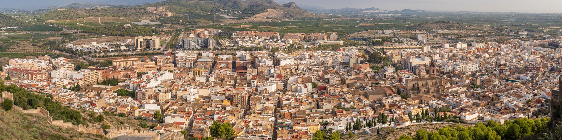 A densely packed cityscape with historical architecture, surrounded by hills and fields.