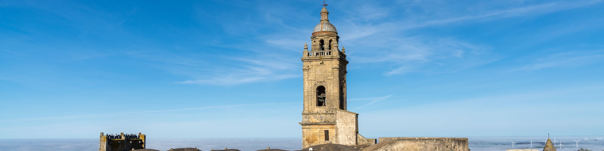 Una torre histórica con cúpula y campana, rodeada de antiguas murallas y un cielo azul despejado.