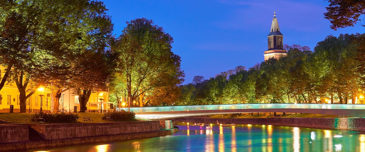 The night panoramic view of Aura river in Turku, Finland with a clock tower of cathedral and bridge on a background.