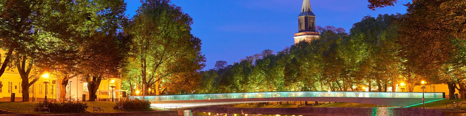 The night panoramic view of Aura river in Turku, Finland with a clock tower of cathedral and bridge on a background.