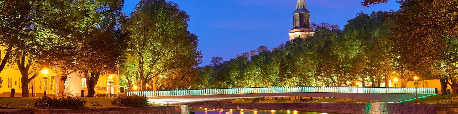 The night panoramic view of Aura river in Turku, Finland with a clock tower of cathedral and bridge on a background.
