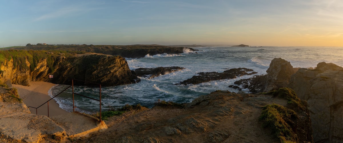 A coastal landscape with rocky cliffs, a sandy beach, and waves crashing against the rocks.