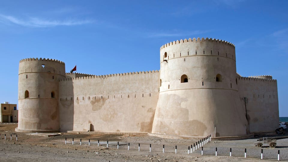 A large, beige fortress with two prominent towers and a flag atop one of them.
