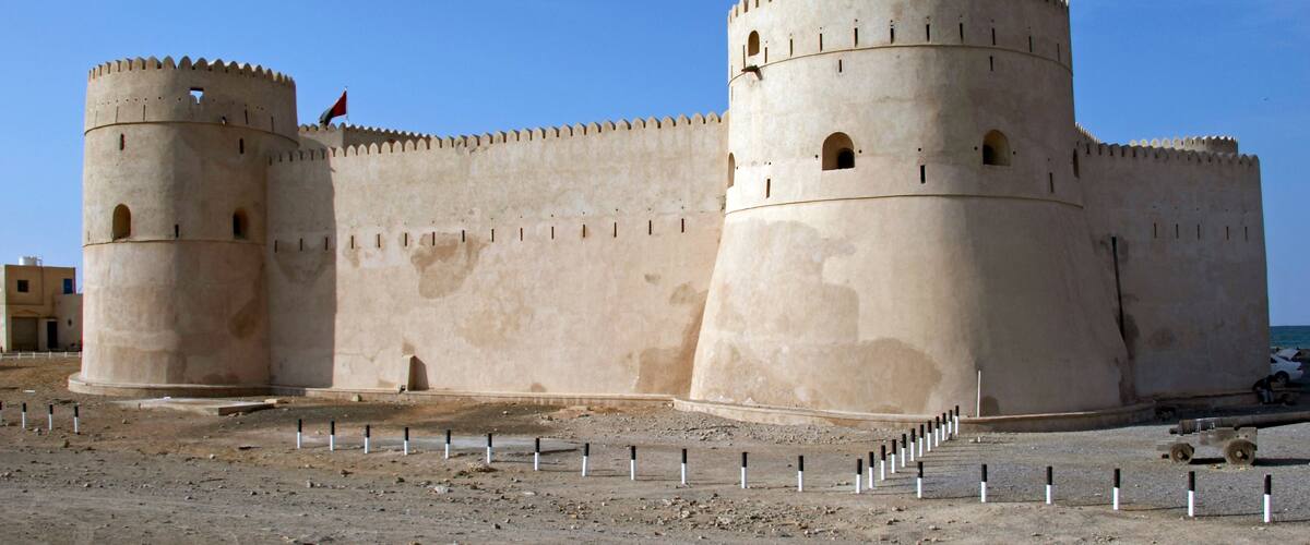 A large, beige fortress with two prominent towers and a flag atop one of them.