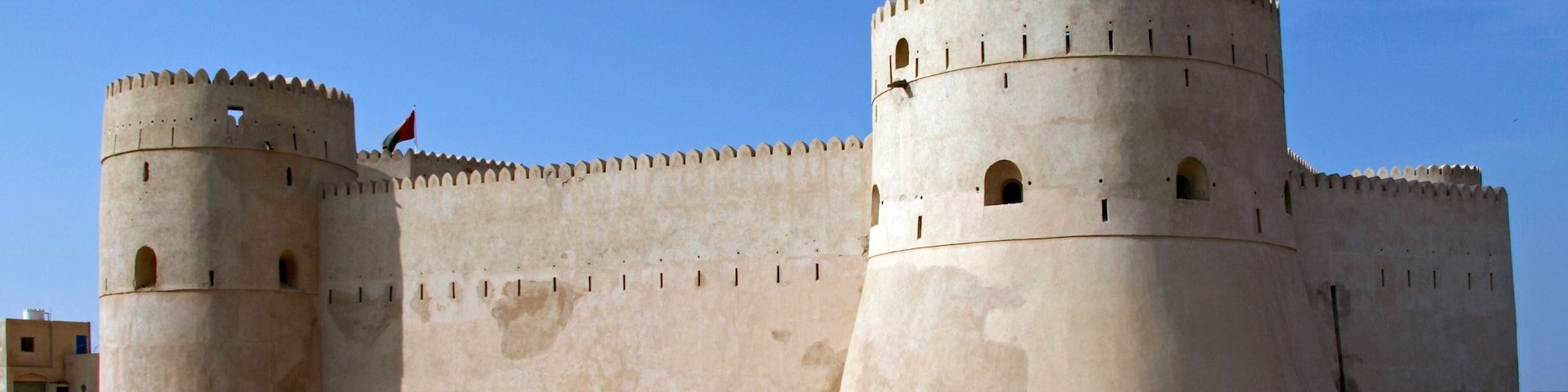 A large, beige fortress with two prominent towers and a flag atop one of them.
