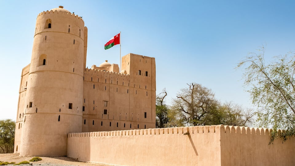 A large, beige fortress with a flag flying atop a tower.