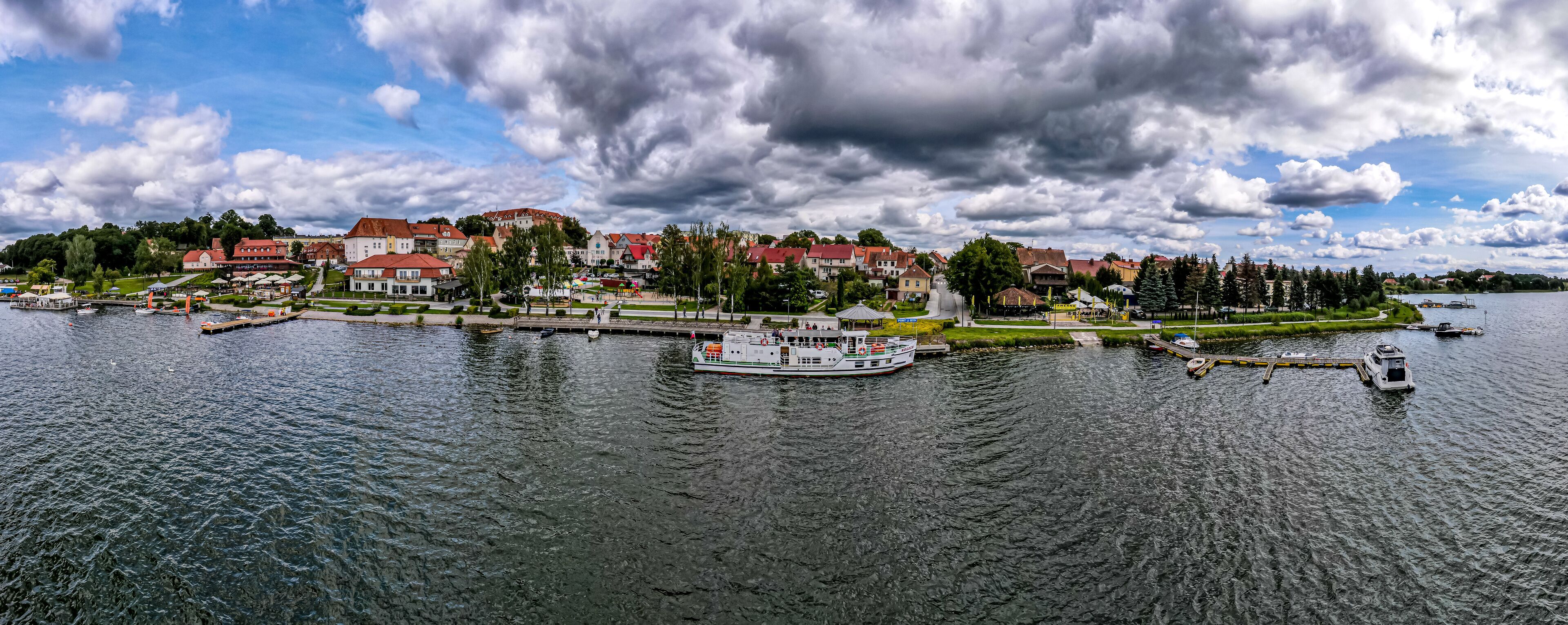 A river with a boat docked at a pier, surrounded by residential buildings and greenery.