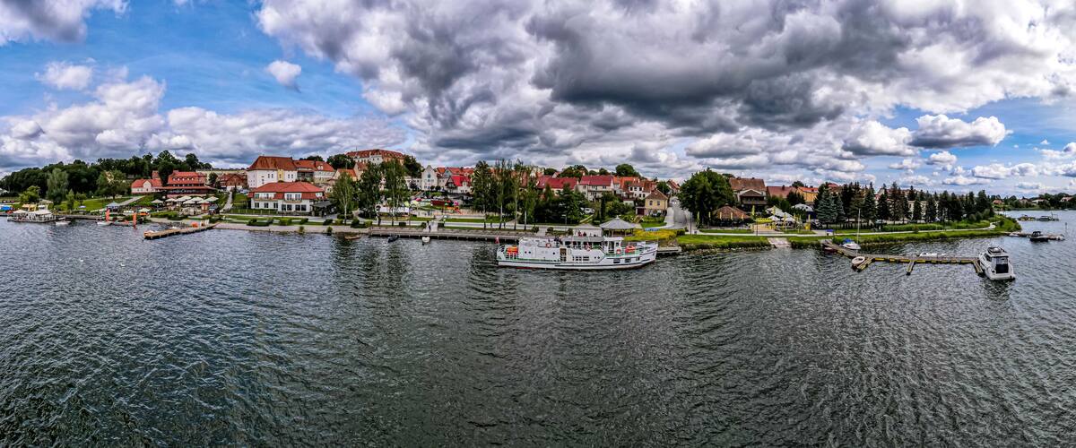 A river with a boat docked at a pier, surrounded by residential buildings and greenery.