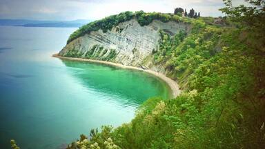 A coastal landscape with cliffs, a beach, and a distant view of mountains.
